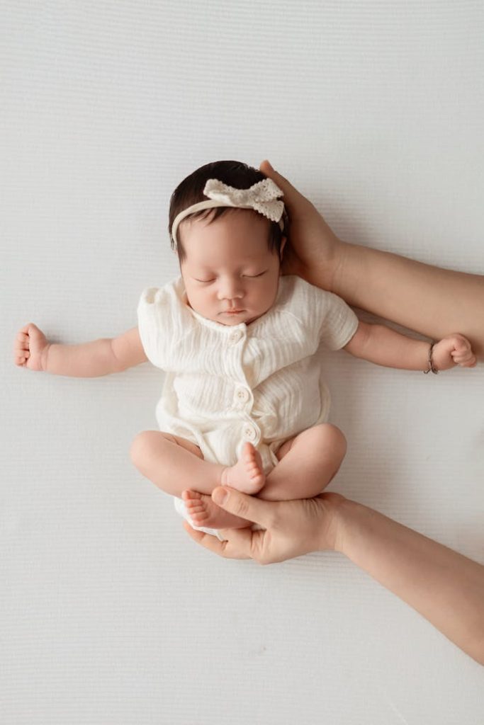 A sweet, sleeping baby wearing a white outfit and bow headband, gently held by hands. Perfect for child and family themes.